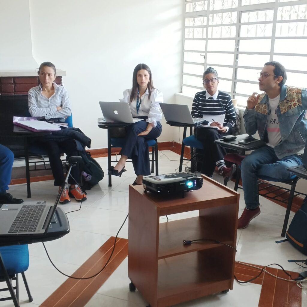 reunión en un salón. En la imagen aparecen 3 mujeres y un hombre. Todos sentados en circulo en torno a un proyector.