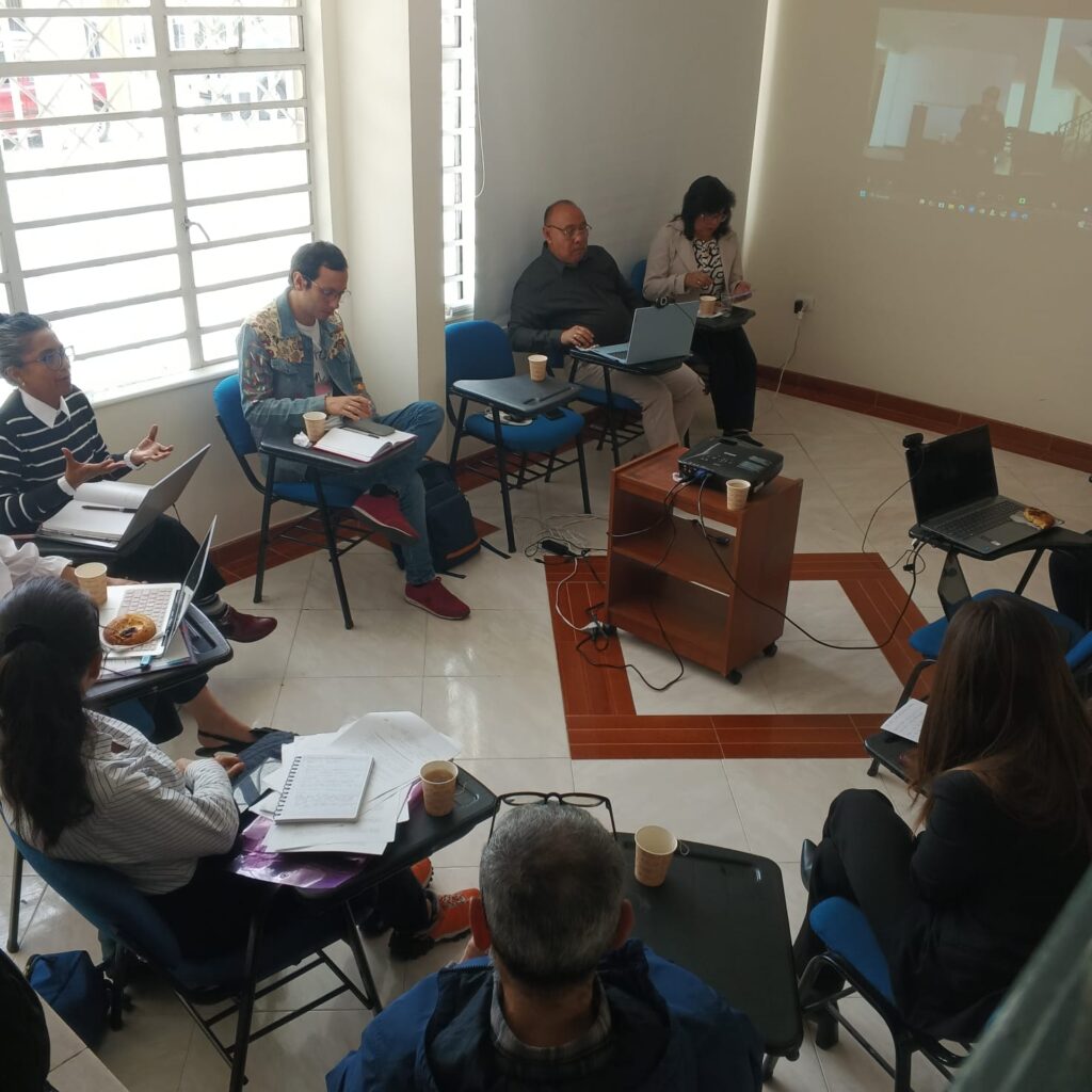 7 personas en una habitación sentadas en torno a un proyector en una reunión